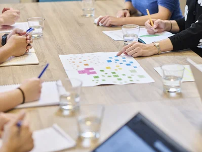 Eine Gruppe von Personen an einem Tisch, die auf ein buntes Diagramm auf Papier zeigen.