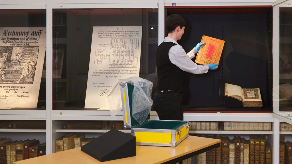 Ausstellungsvorbeitung an der SUB Göttingen Restauratorin legt ein Buch in eine offene Vitrine; daneben geschlossene Vitrinen mit Faksimiles.