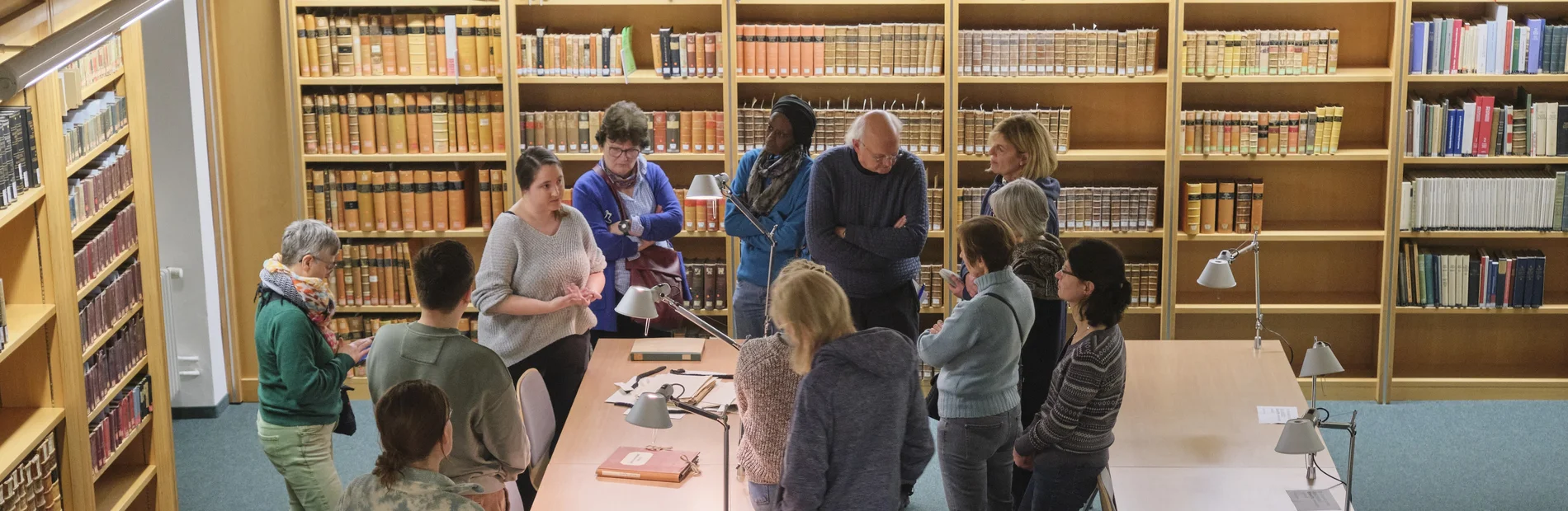 Einführung in die Benutzung von Altbeständen Ein Vortrag vor historischen Büchern, dem eine Gruppe von Menschen aufmerksam folgt