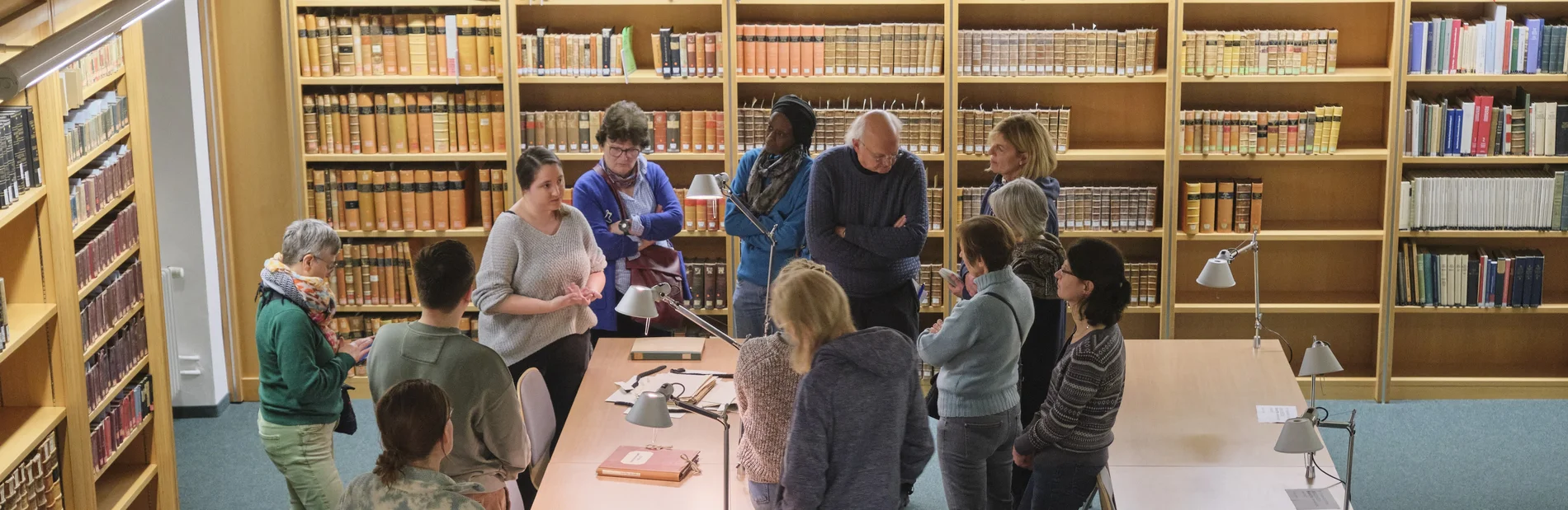 Einführung in die Benutzung von Altbeständen Ein Vortrag vor historischen Büchern, dem eine Gruppe von Menschen aufmerksam folgt