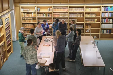 Ein Vortrag vor historischen Büchern, dem eine Gruppe von Menschen aufmerksam folgt