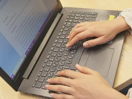 Eine Person arbeitet am Laptop. Auf dem Bildschirm ist eine Textdatei geöffnet.