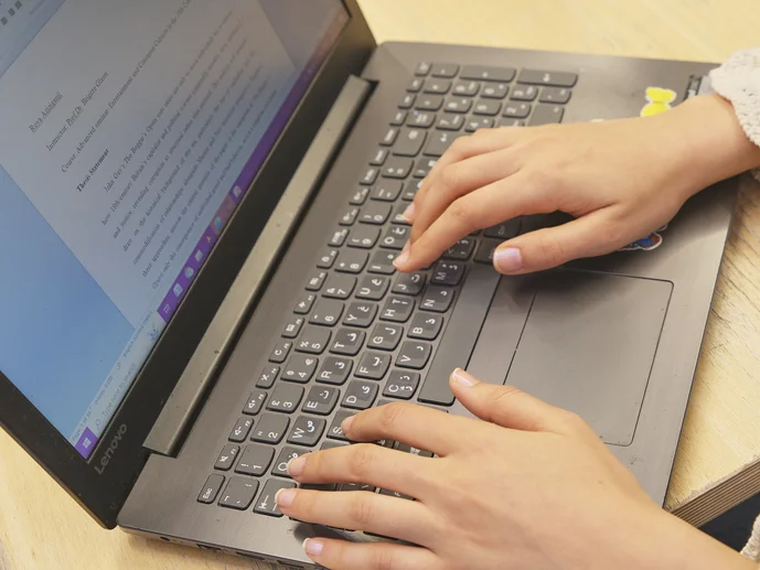 Eine Person arbeitet am Laptop. Auf dem Bildschirm ist eine Textdatei geöffnet.