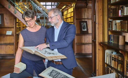 Beratung zu historischen Beständen an der SUB Göttingen Zwei Personen im historischen Bibliothekssaal, eine zeigt der anderen ein altes Buch