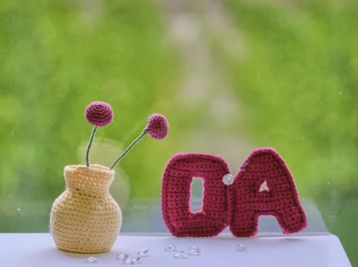 Gehäkeltes OA-Symbol und Blumenwase auf grünen Hintergrund