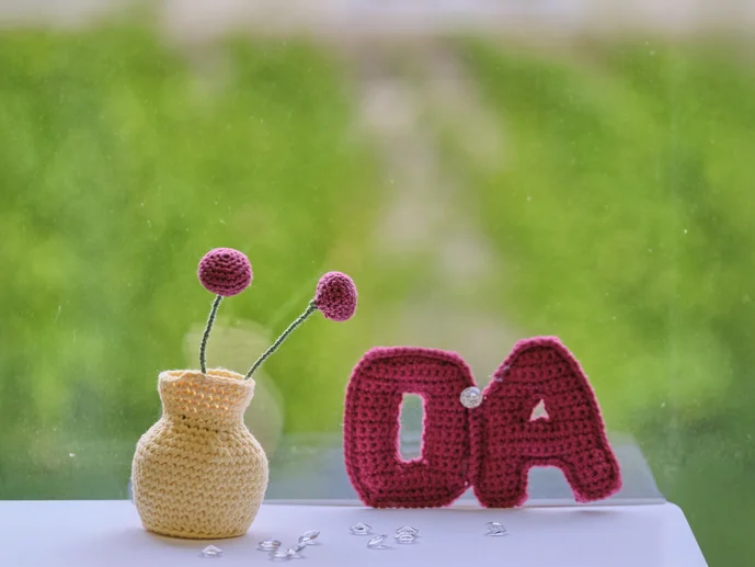 Gehäkeltes OA-Symbol und Blumenwase auf grünen Hintergrund